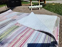 Large cotton bedspread with multi-color segmented stripes and stitched quilting visible on both sides, laid flat outside for display.
