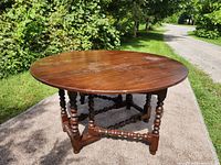 Round dining table on outdoor pavement, showing top with circular shape and turned legs in dark wood finish.