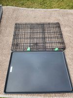 Top view of a black metal wire dog crate with removable plastic tray base on carpet.