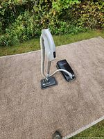 Full view of Kenmore Wispertone vacuum cleaner standing upright on a beige carpet outdoors showing hose and main vacuum body.