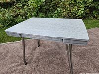 Full front side angle of retro kitchen table showing light gray patterned Formica tabletop and chrome legs.