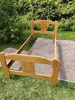 Single wood bedframe assembled outdoors on grass with a mat underneath, showing headboard and footboard connected by side rails.