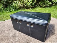 Black faux leather storage tote closed, showing stitched detailing and metal grommets on the front panel, placed outdoors on a concrete surface.
