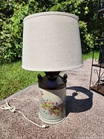 Full view of the ceramic table lamp with floral hand-painted design and neutral fabric lampshade outdoors on a stone surface.