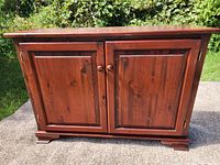 Front view of closed cabinet showing two paneled doors with wooden knobs and decorative feet base.