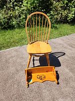 Wooden chair with spindle back and ornate wooden wall shelf on the ground in front of chair.