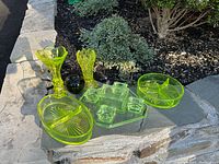 Overview of all five uranium depression glass pieces arranged on stone slab: two vases at rear, two oval dishes front, smoker set center
