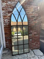 Full front view of arched mirror leaning against brick wall