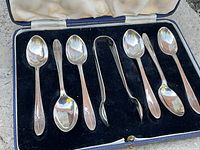 Sterling silver teaspoons and sugar tongs arranged inside blue velvet-lined box, showing design and condition of flatware
