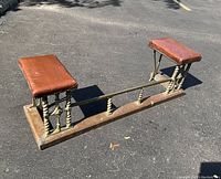 Full view of brass and brown leather club fender on asphalt background, showing two leather padded rests and brass rail