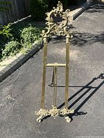 Front view of full easel on driveway, showing top ornament, upright supports, and decorative feet