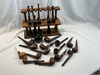 Photo showing two-tiered wooden pipe stand with 12 pipes held vertically and 12 additional pipes laid out in front along with a green apple used for sizing reference.