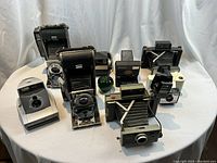 Overview of eight Polaroid cameras arranged on white fabric backdrop, front angle view
