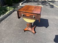Front left perspective view of closed drop leaf rosewood sewing table on octagonal pedestal and splayed base