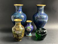 All four cloisonne vases shown together with a green glass apple for size reference. Two taller matching blue baluster vases are behind, a medium yellow-green-russet floral vase to the left front, and a small blue floral vase to the right front.
