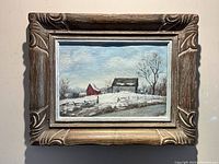 Front view of framed oil painting depicting a winter landscape with red barn and grey shed under a pale sky
