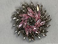 Top view of brooch showing spiral arrangement of pink and clear crystals on grey background