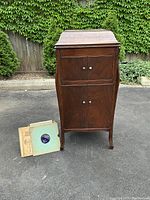 Front view of closed mahogany-finish wood cabinet with a stack of shellac records alongside