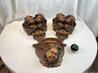 Three carved wooden corbels displayed on white backdrop with green apple for size reference