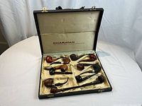 Vintage Charatan presentation box open showing twelve briar tobacco pipes on cream satin lining