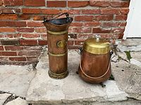 Photo of two antique heavy gauge copper and brass pots on stone floor with brick wall background.
