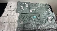 Photo showing multiple white and sage green women's tops with tags from Maurices, size medium, sealed in plastic and laid flat.