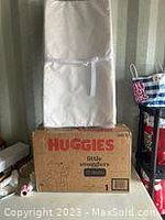 Photo showing white baby changing pad placed on top of large Huggies diaper box.
