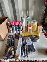 Photo showing BMW motor oil, Axe oil cans, Quick Mark spray cans, permanent sealer tubes, adhesive tapes, paint brushes, and construction plastic sheeting on a surface.