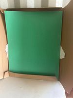 Top view of a stack of green Bristol board sheets inside a cardboard box.
