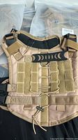 Front view of a tan colored tactical style puppy vest showing velcro front panel with attachment loops and adjustable straps with buckles