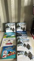 Two copies of 'Gwerf' by Larry MacDougall and several other hardcover children's books arranged on a table.