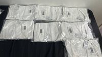 Seven white tank tops for women size large, each sealed individually in plastic packaging and laid out on a surface.