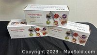 Three boxes of stainless steel potato presses stacked together on a black surface, showing the product name and images of pressed foods.