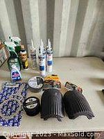 Wide view of shop lot showing bottles of adhesives, cleaning solutions, multiple tubes of caulking, rolls of plumbing tape, black plastic fittings, and a small bottle of glue.