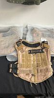 Photo showing four new tan tactical style small puppy vests with one vest displayed on top