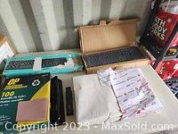View of two keyboards, file folders, staplers, 3-hole punch, and packaged printer paper on a table.