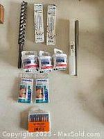Photo showing drill bits and packs of saw blades and razor blades on a light surface.