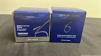 Front view of ZO Skin Health Growth Factor Serum and Complexion Renewal Pads boxes side by side on a light surface.