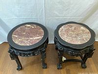 Two carved wood stools with round marble tops side by side, front view.
