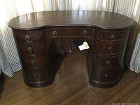 Front view of kidney-shaped desk showing eight drawers and brass ring pulls