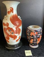 Photo of large white vase with red dragon and smaller black dragon vase together on table