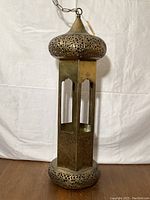 Full view of the tall Moroccan style brass hanging lamp with domed top, rectangular body, and round base.