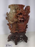 Front view showing tall soapstone vase with carved potted flowers and bird, with wooden stand and visible chip on leaf.