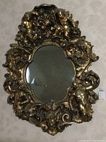 Full view of vintage Baroque-style wall mirror with gold gilt deep relief frame featuring cherubs and floral motifs.