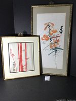 Two framed Japanese art prints displayed against a dark background, one with red bamboo stalks and the other with orange tiger lily flowers.