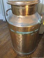 Front and side view of copper milk jug, showing brass straps and handles, with visible patina and verdigris developing under straps.