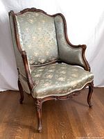 Front and left side view showing green silk fabric with floral pattern and carved wooden frame.