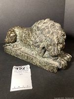 Front-right perspective of recumbent marble lion on rectangular base showing head, mane and front paws