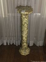 Full view of the tall marble pedestal showing the column and octagonal top against sheer curtains.