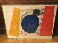 Framed abstract artwork with yellow, blue, and red shapes within a silver frame against wood floor
